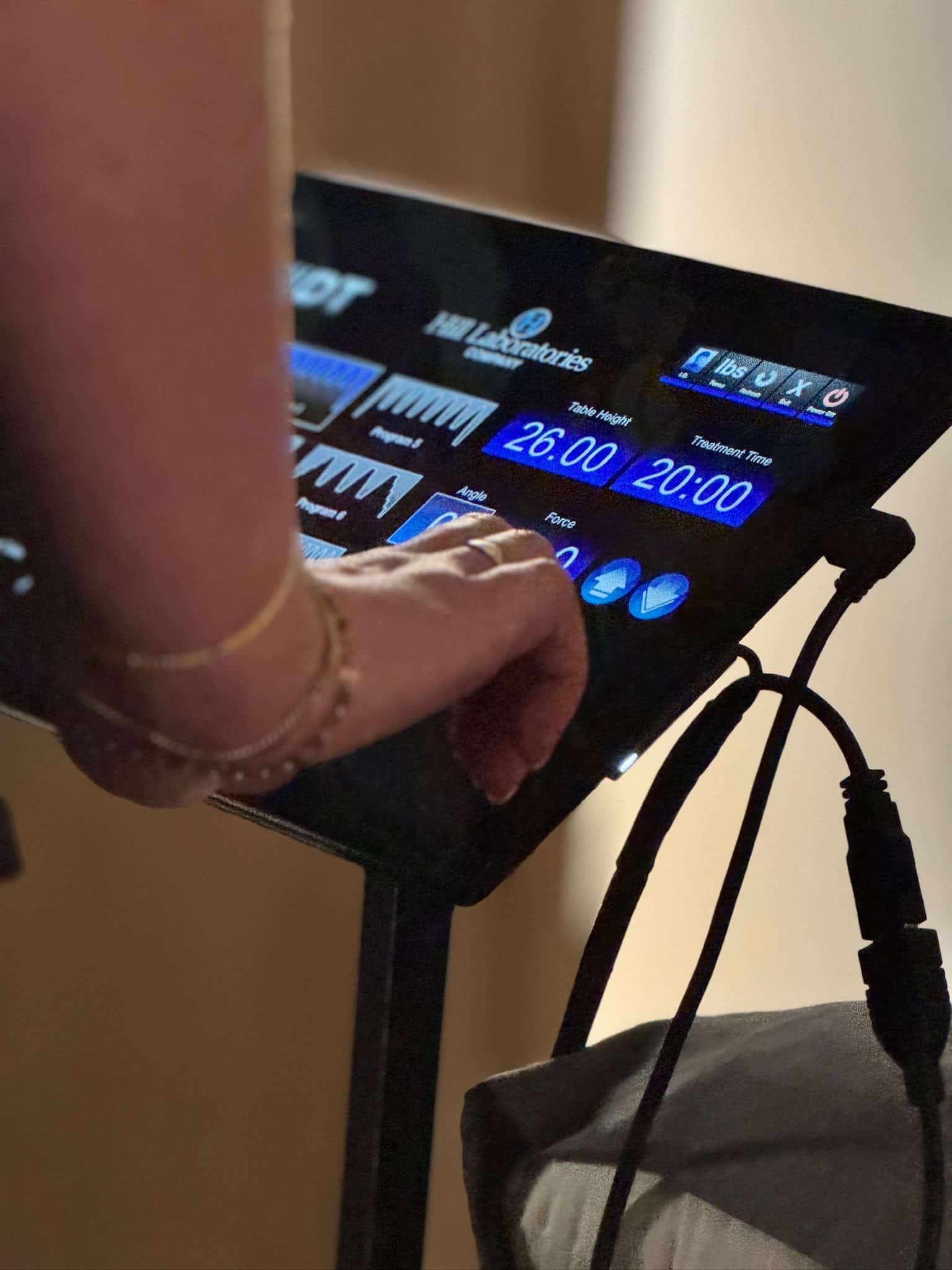 Close-up of a patient's hand adjusting settings on a hill laboratories spinal decompression machine control panel in the clinic.