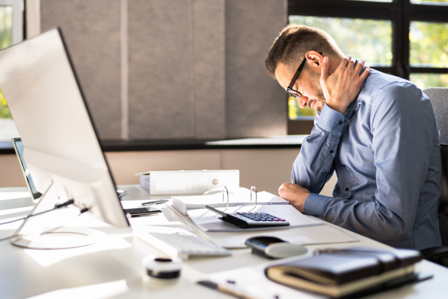 a man with poor posture sitting at a desk with his hand on his neck