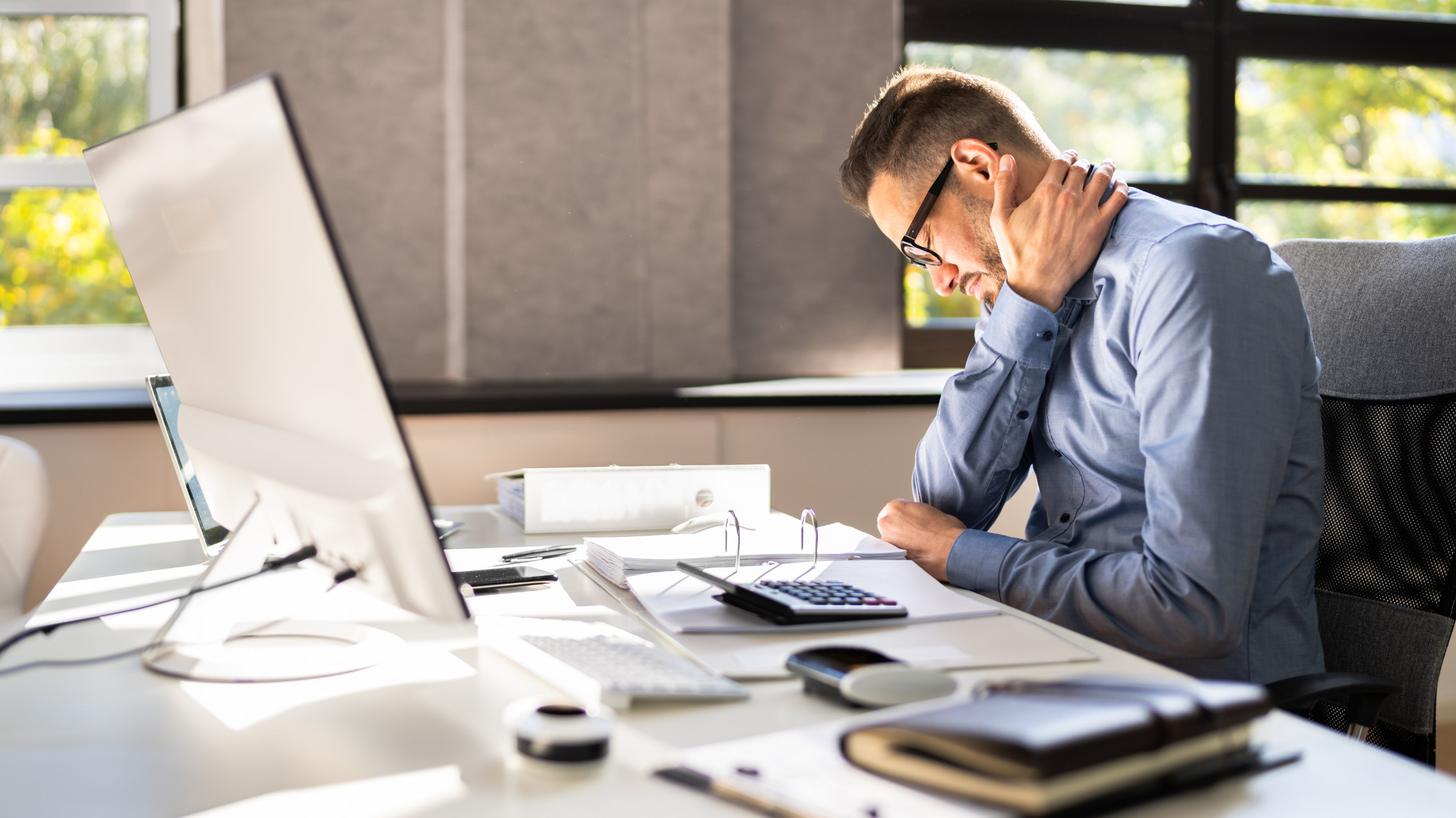 a man with poor posture sitting at a desk with his hand on his neck