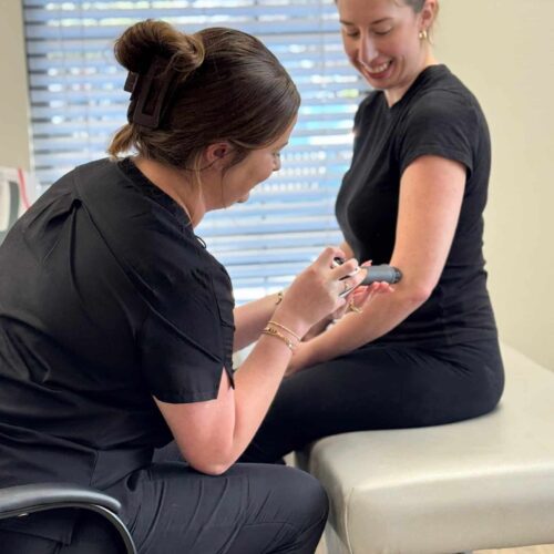 Brittany sits in a chair next to a patient seated on the treatment table