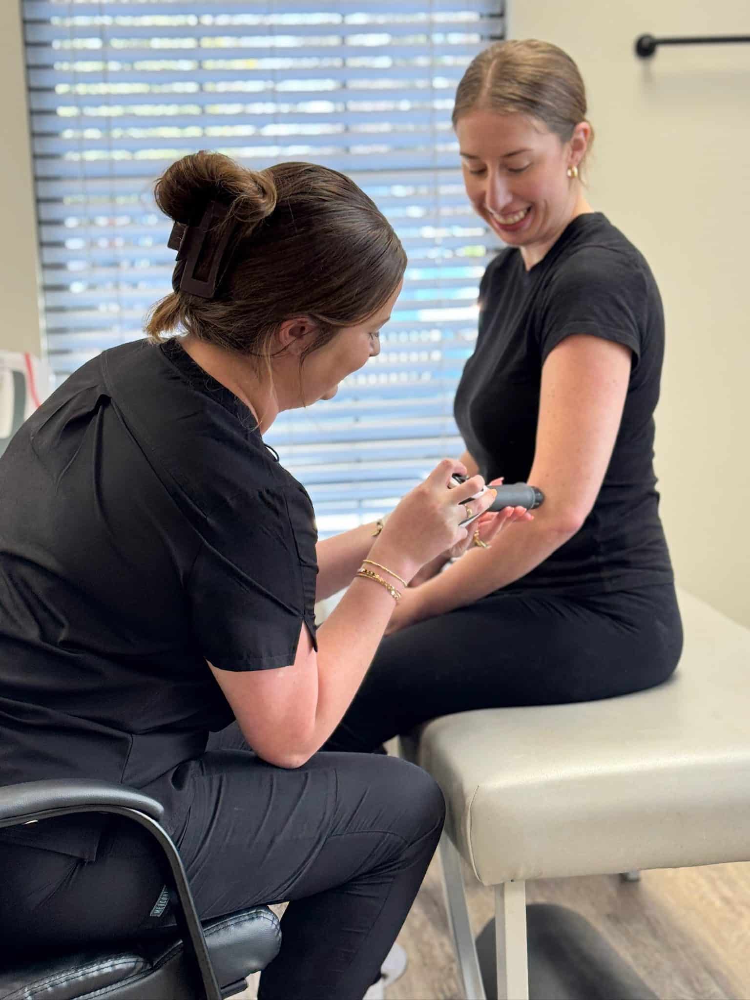 Brittany sits in a chair next to a patient seated on the treatment table