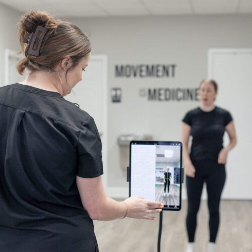 Brittany stands behind a tablet on a stand that displays a patient’s movement assessment.