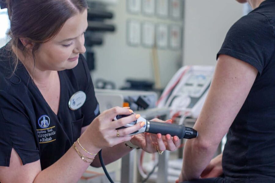Brittany sits beside a patient on the treatment table, pointing to a printed exercise sheet while explaining a customized home exercise and rehab program.