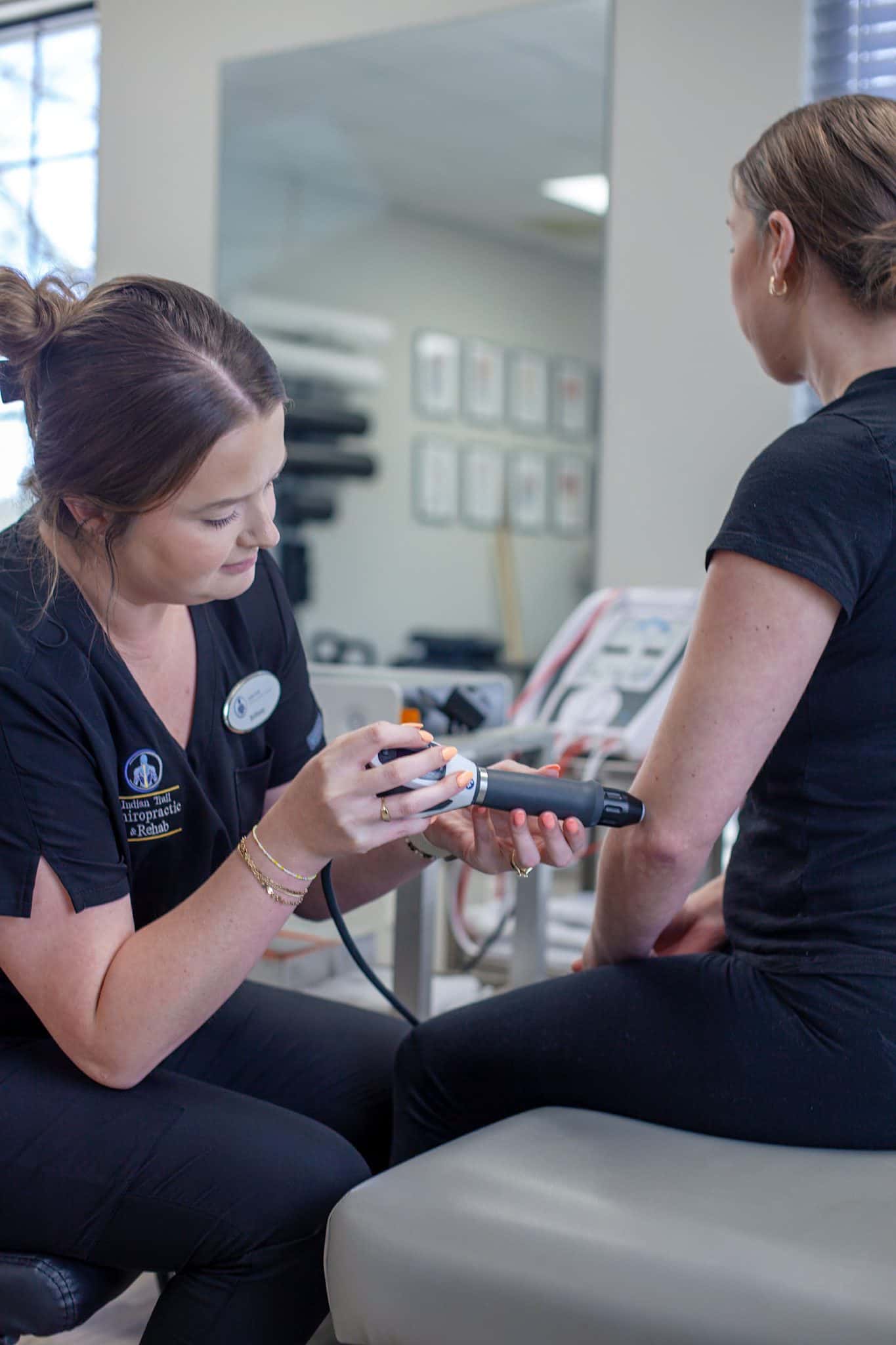 Brittany sits beside a patient on the treatment table, pointing to a printed exercise sheet while explaining a customized home exercise and rehab program.