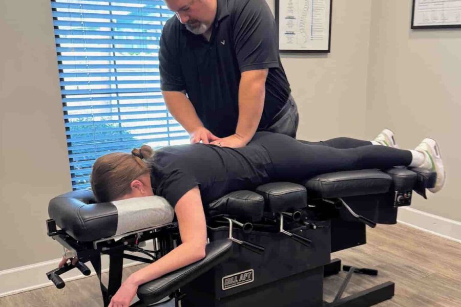 Wide view of Dr. Cameron Gentile delivering a chiropractic adjustment as the patient lies face down on the treatment table in a bright exam room.