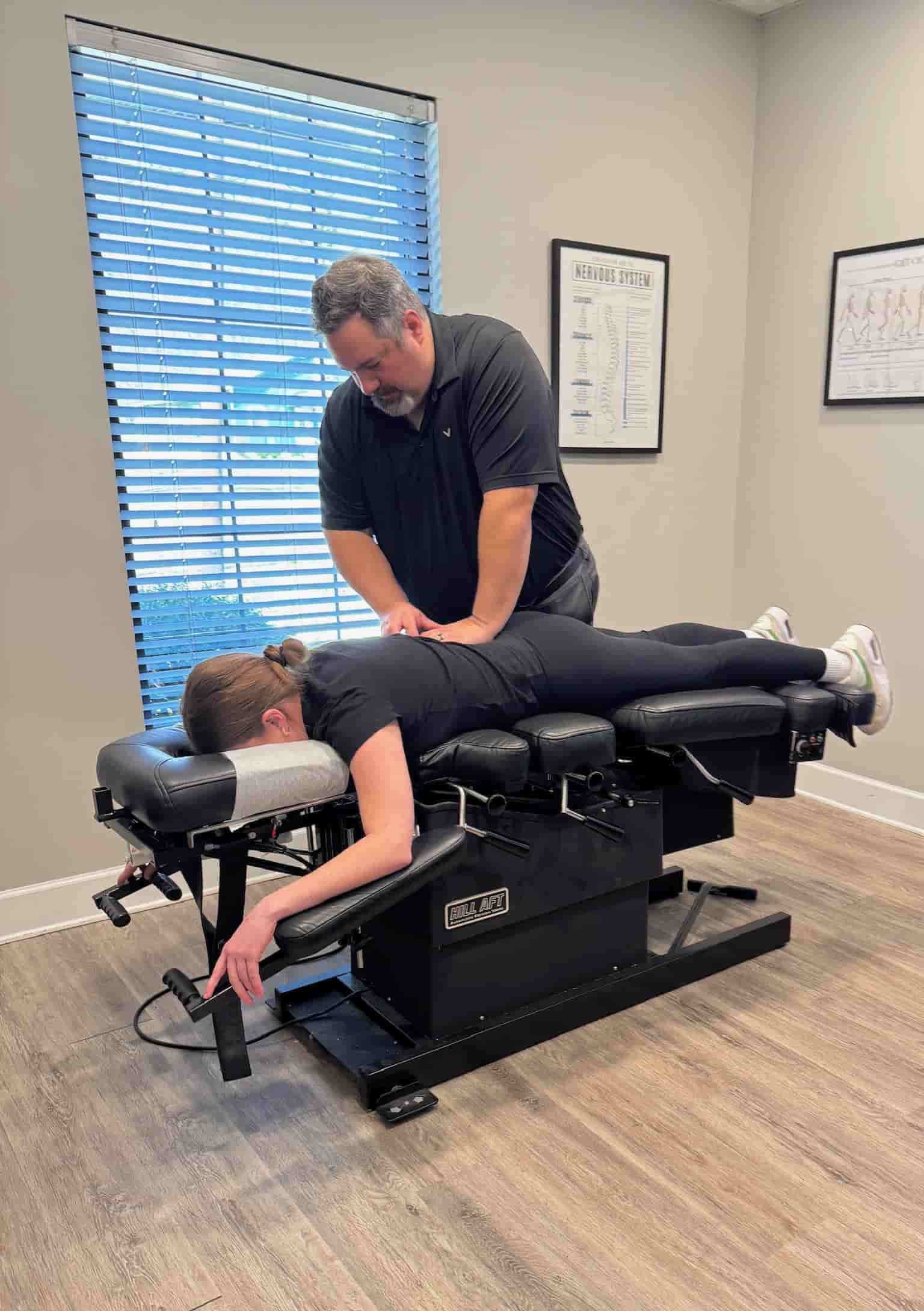 Wide view of Dr. Cameron Gentile delivering a chiropractic adjustment as the patient lies face down on the treatment table in a bright exam room.