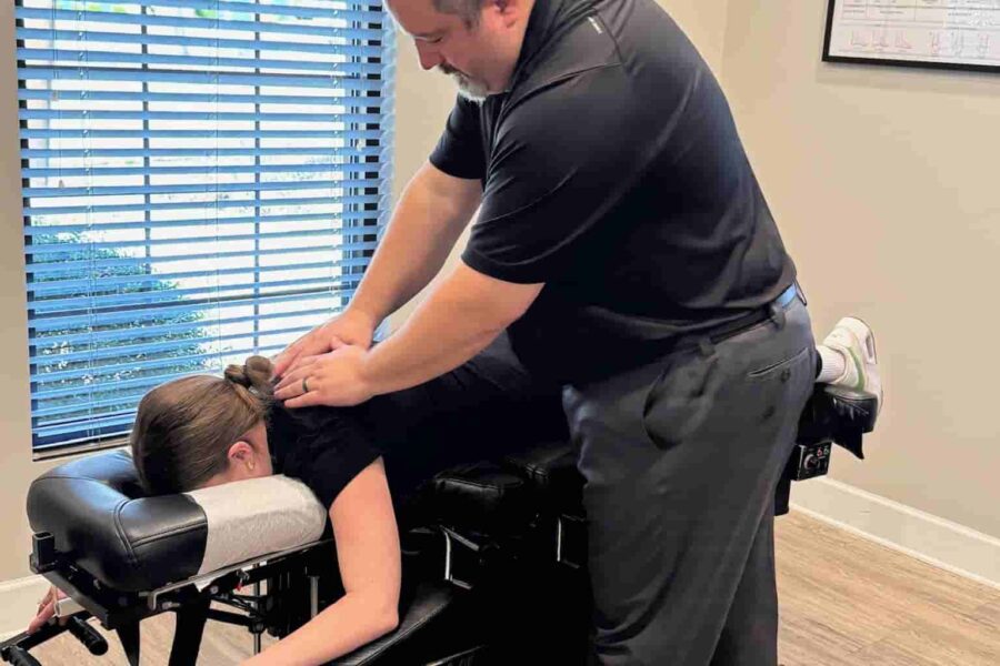Dr. Cameron Gentile stands over a patient on a drop‑style chiropractic table, applying a thoracic adjustment with his hands on the patient’s lower back.