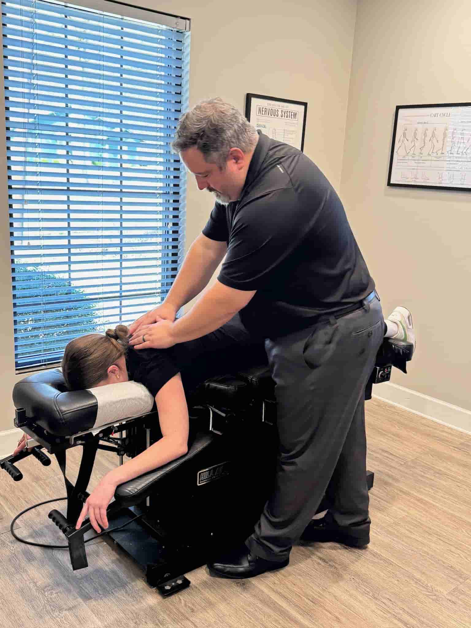 Dr. Cameron Gentile stands over a patient on a drop‑style chiropractic table, applying a thoracic adjustment with his hands on the patient’s lower back.