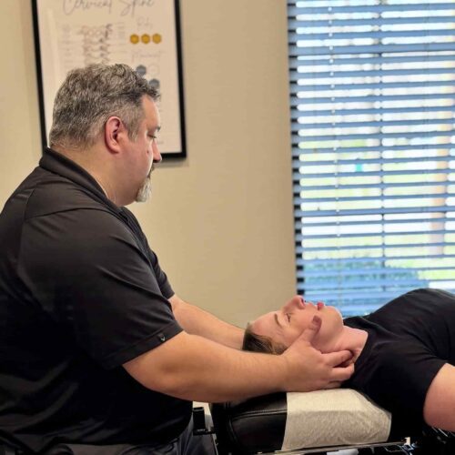 Dr. Cameron Gentile supports the patient’s head and neck with both hands while performing a chiropractic cervical adjustment on the treatment table.