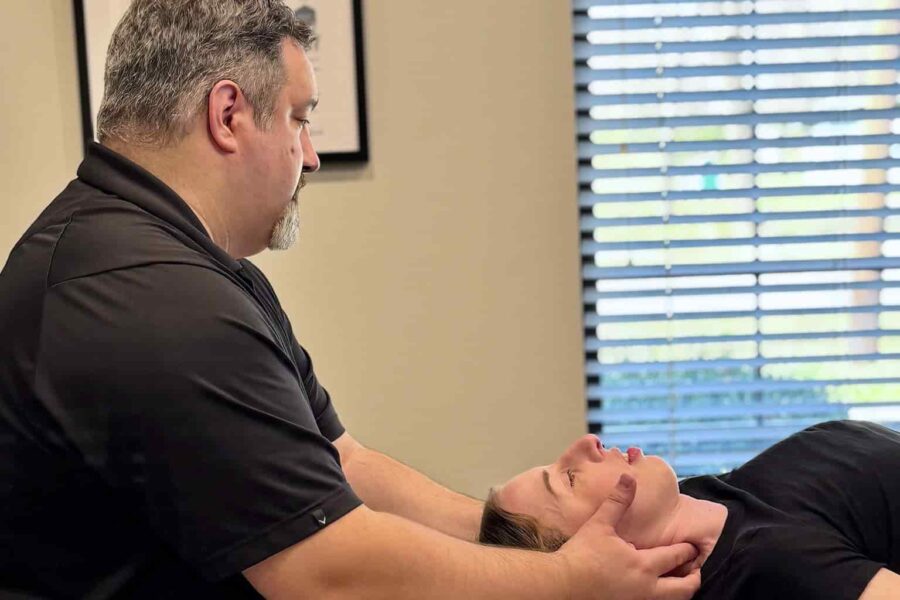 Dr. Cameron Gentile supports the patient’s head and neck with both hands while performing a chiropractic cervical adjustment on the treatment table.