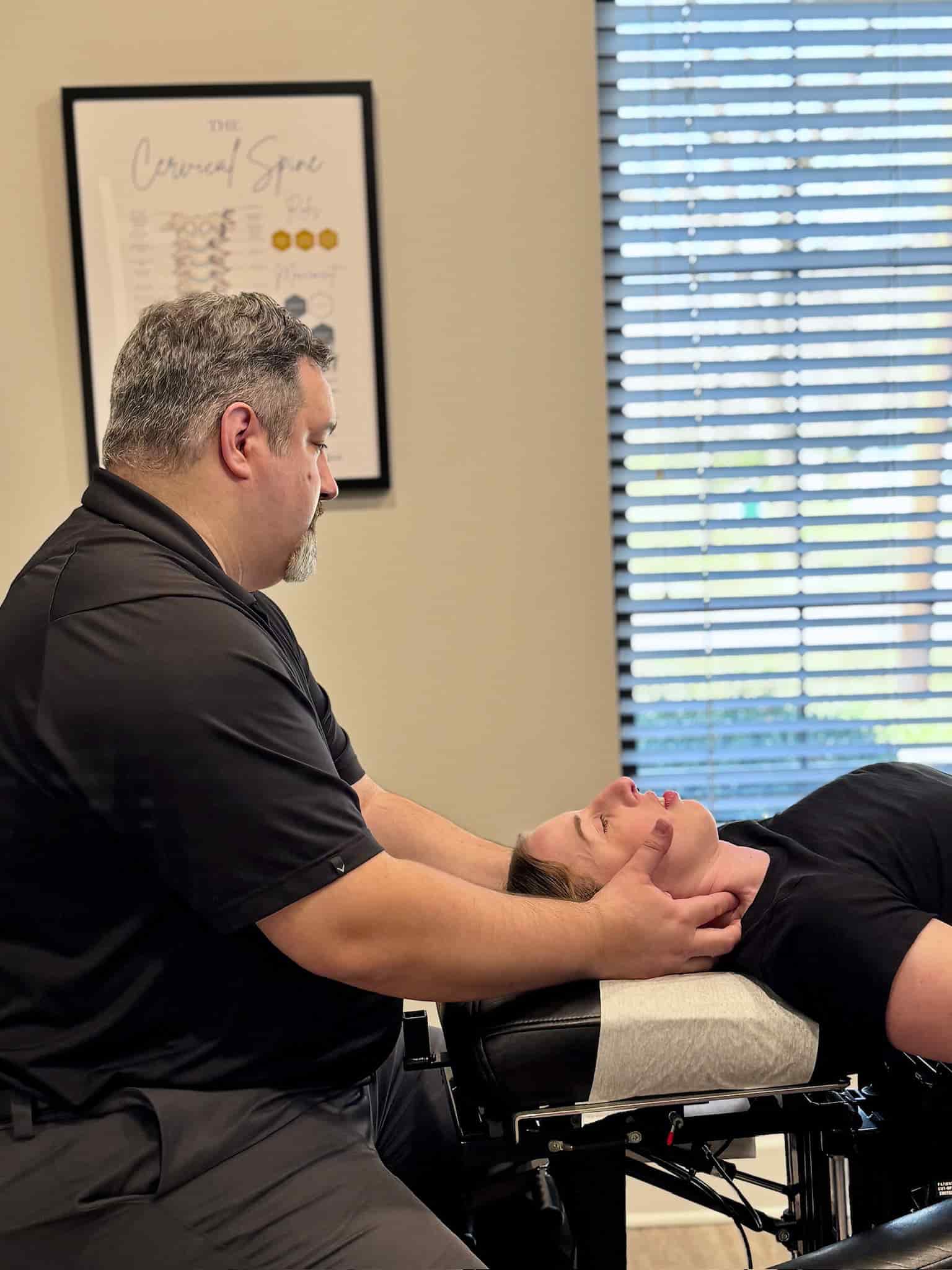Dr. Cameron Gentile supports the patient’s head and neck with both hands while performing a chiropractic cervical adjustment on the treatment table.