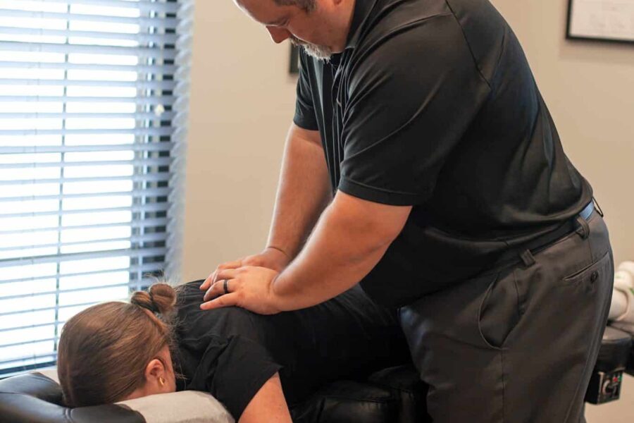 Dr. Cameron Gentile stands beside a chiropractic table, positioning his hands on a patient’s neck and upper back while they lie face down for an adjustment.