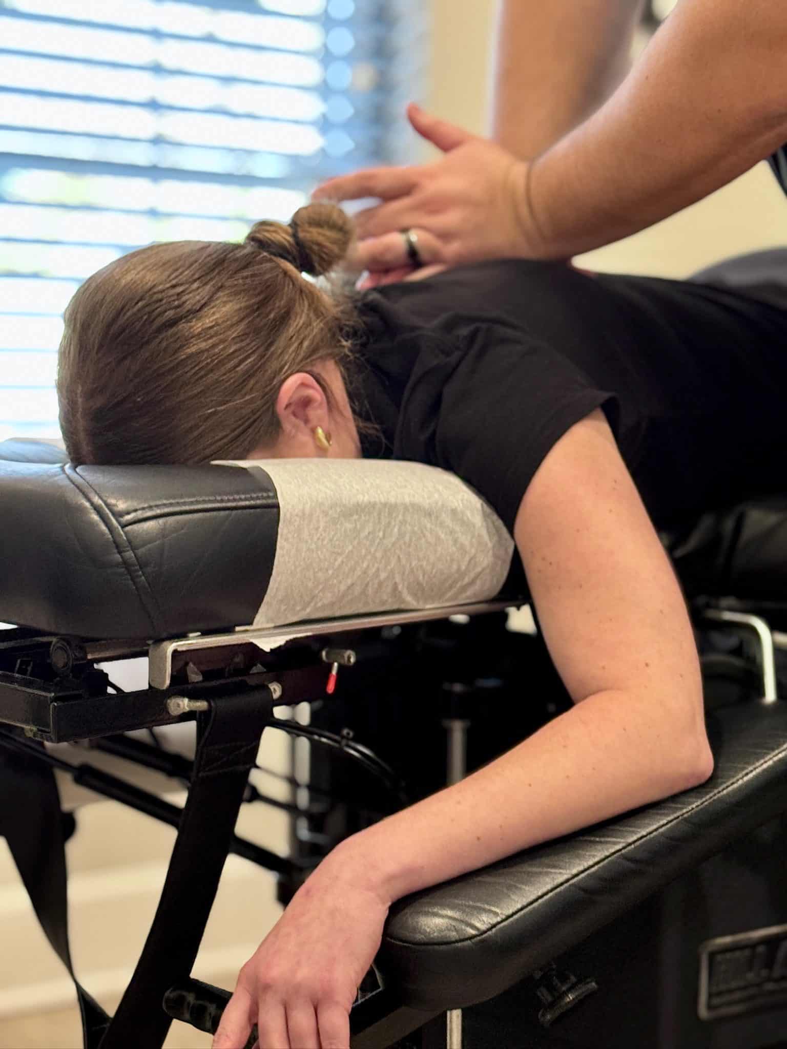 Close-up of a patient lying face down on a chiropractic table while Dr. Cameron Gentile places his hands on the upper back to deliver a thoracic adjustment.