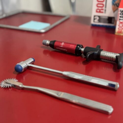 Several handheld chiropractic and soft tissue instruments are laid out on a red countertop in the treatment room.