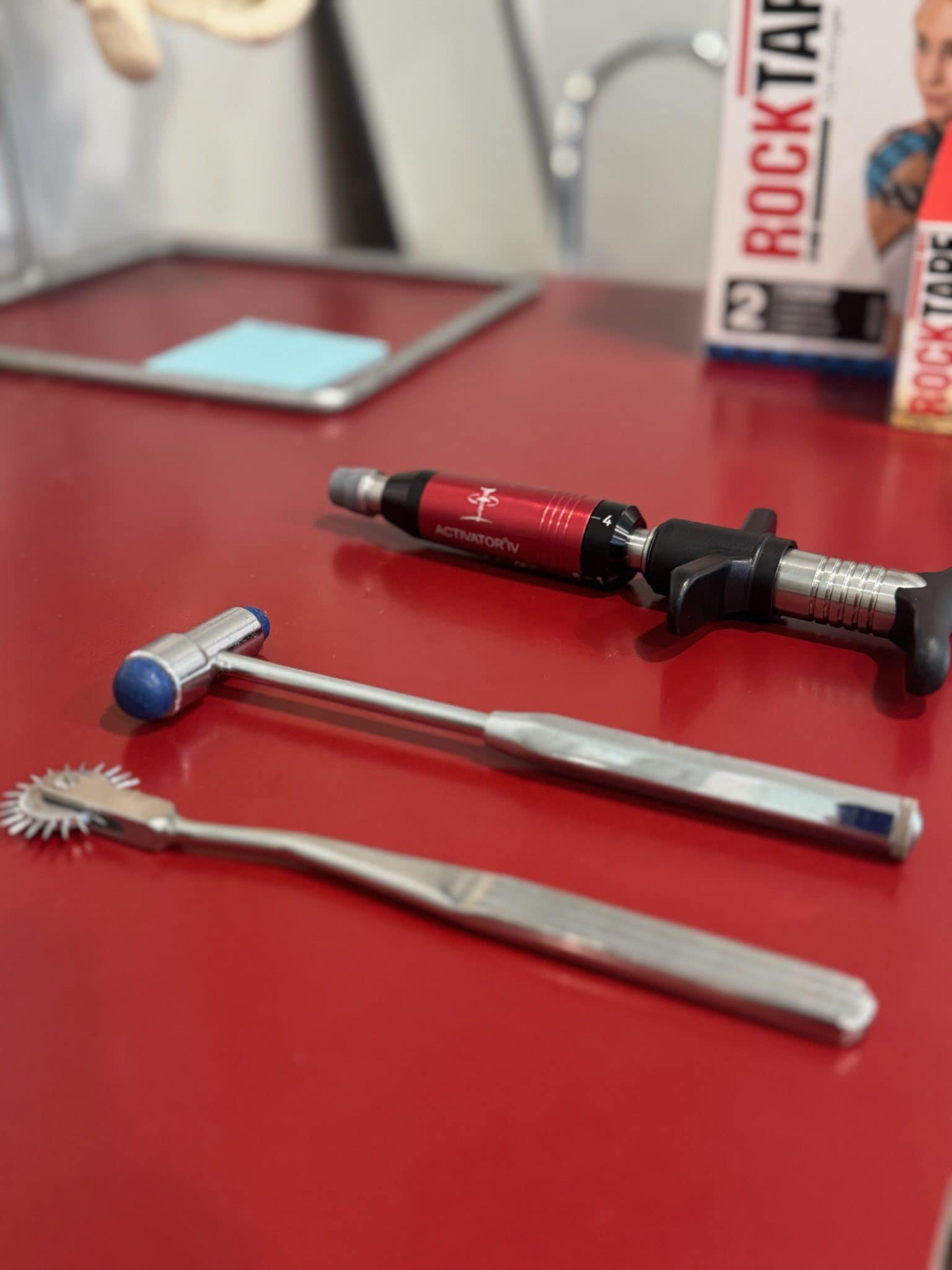 Several handheld chiropractic and soft tissue instruments are laid out on a red countertop in the treatment room.