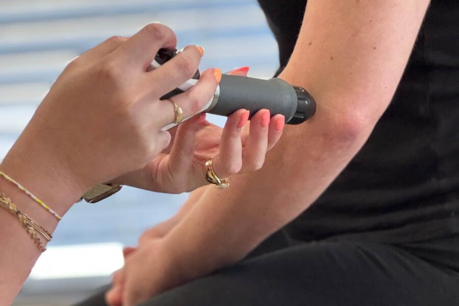 Close-up of a clinician holding a small handheld therapy tool against a patient’s forearm during a soft tissue treatment.
